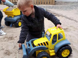 Kind speelt met een speelgoedtrekker in het zand.