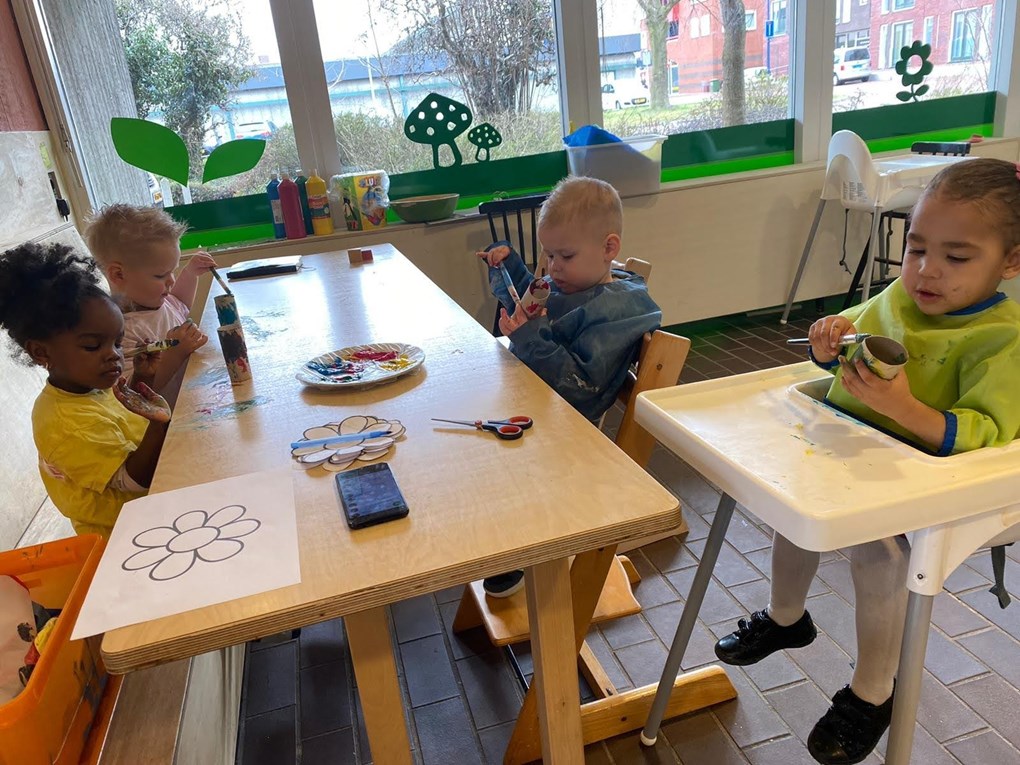 Kinderen schilderen wc-rolletjes aan tafel.